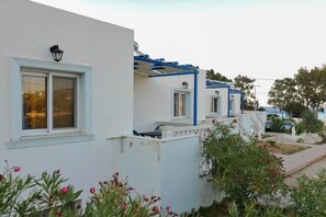 A row of white buildings with blue accents, small windows, and a garden area with pink flowers.