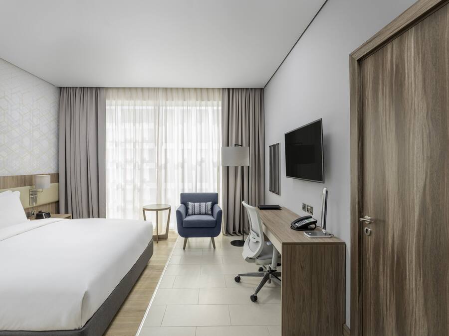 Quarto de hotel com cama grande, secretária com computador, cadeira, televisão e guarda-roupa.