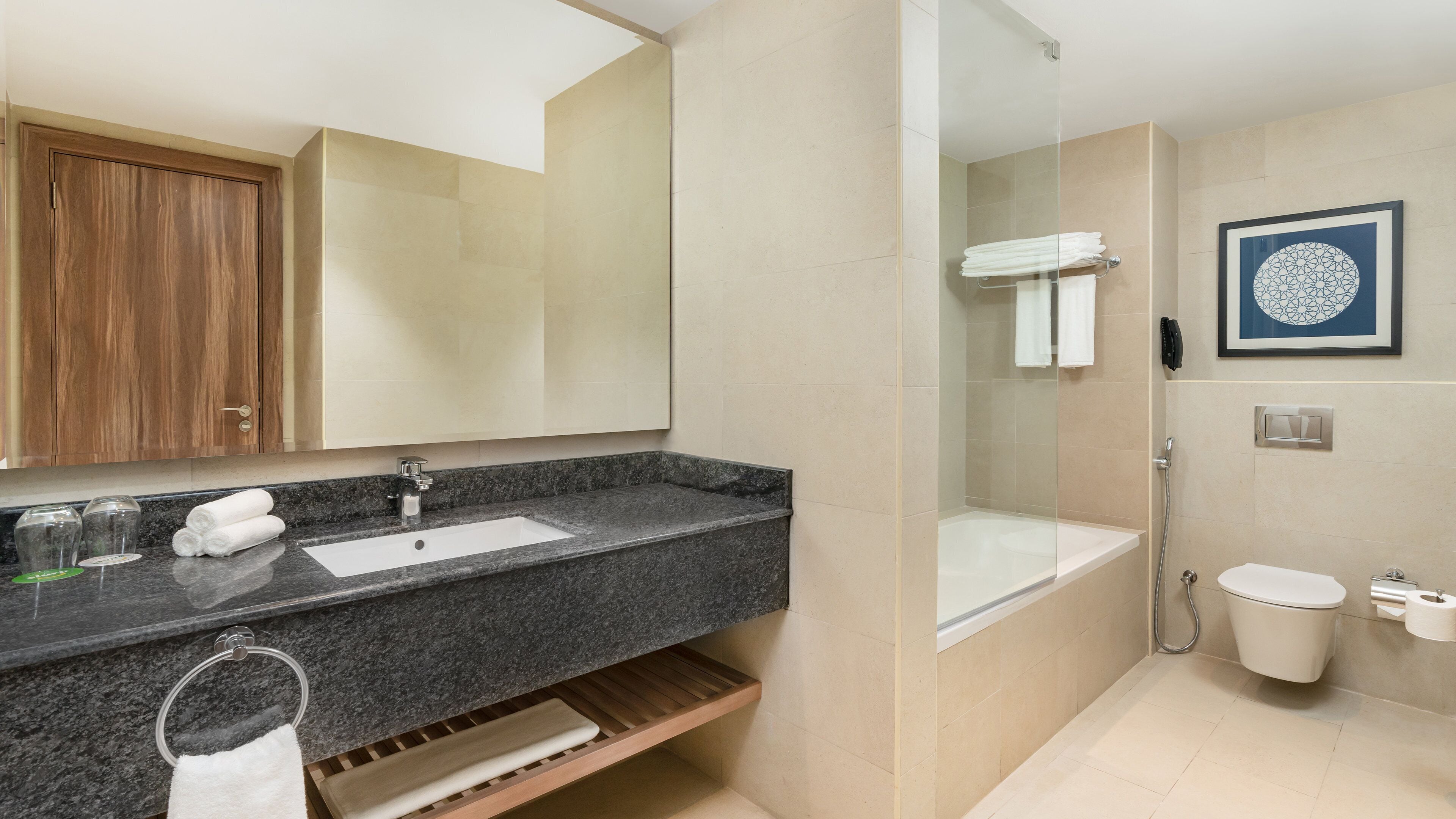 Un baño moderno con encimera de granito, lavabo, espejo, ducha e inodoro.