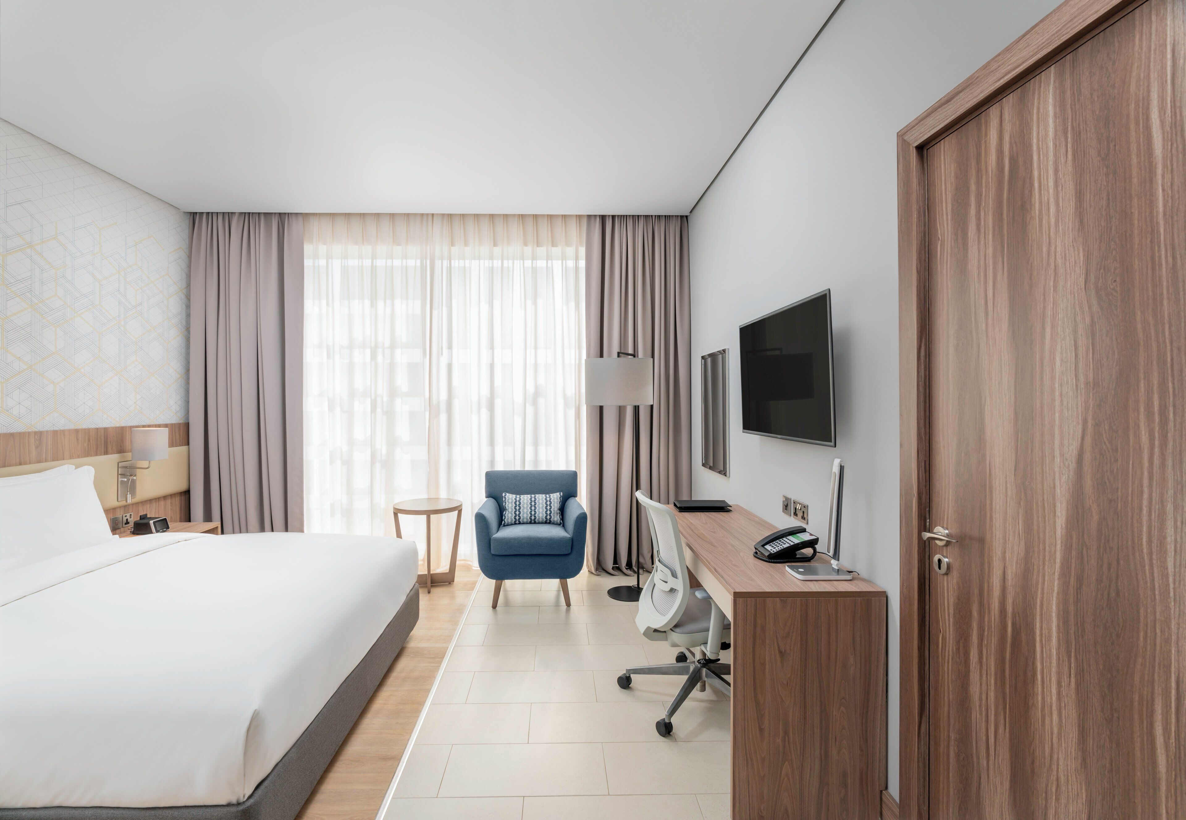 Una habitación de hotel con cama, escritorio con computadora, silla, televisor y armario.