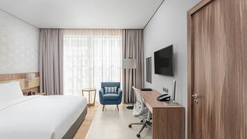 Una habitación de hotel con cama, escritorio con computadora, silla, televisor y armario.