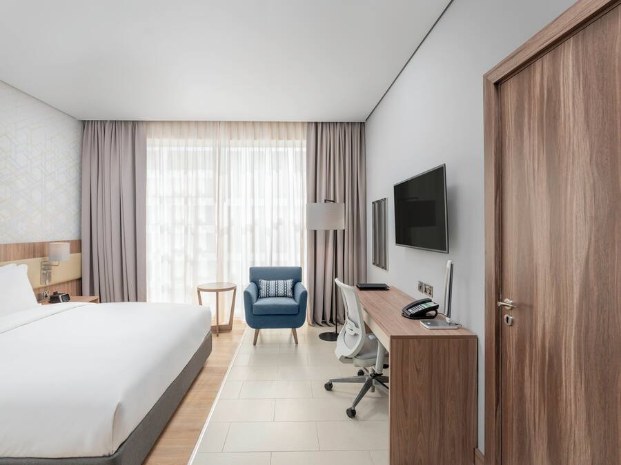 Una habitación de hotel con cama, escritorio con computadora, silla, televisor y armario.