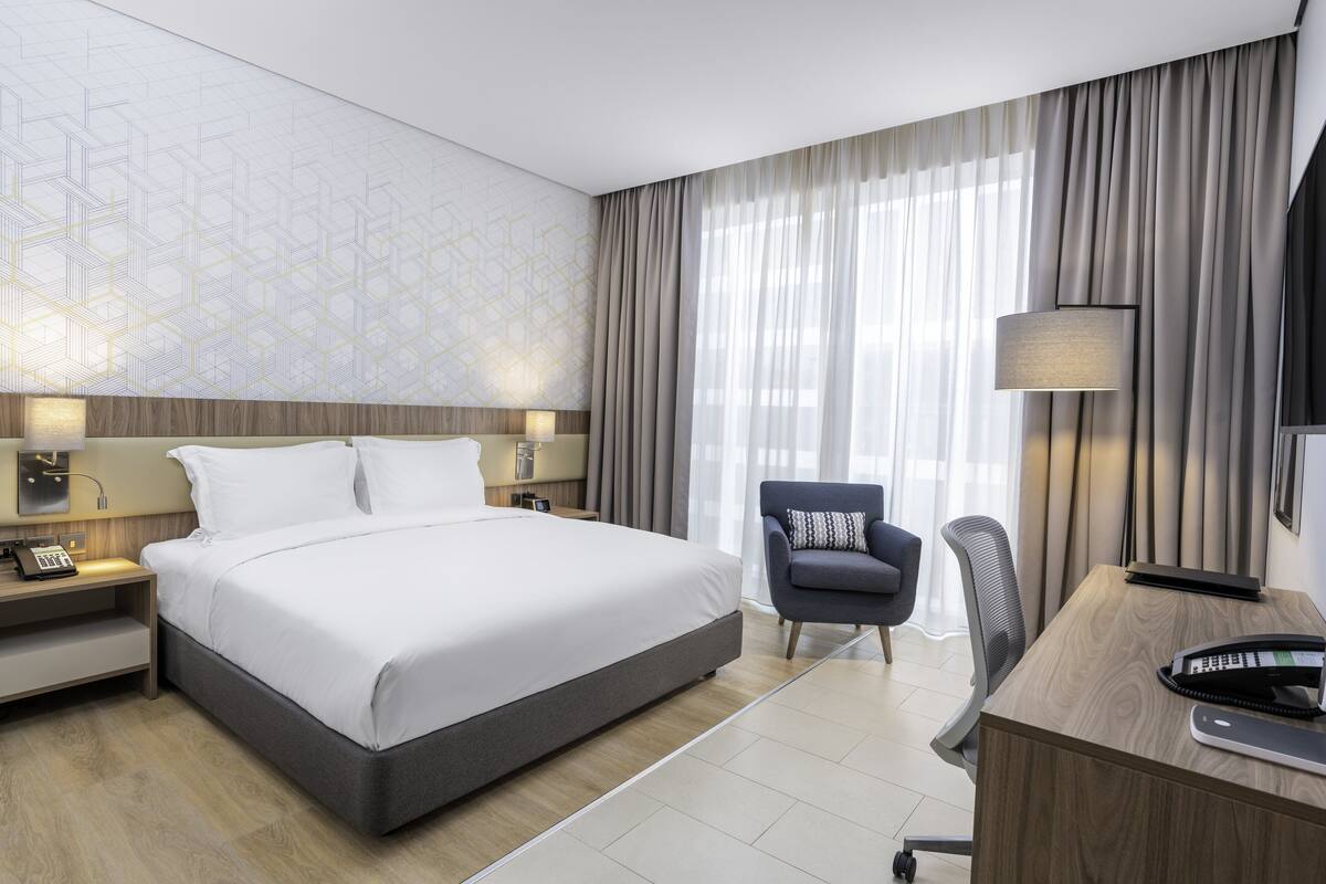Ett modernt hotellrum med en stor säng, ett skrivbord, en stol och en lampa.