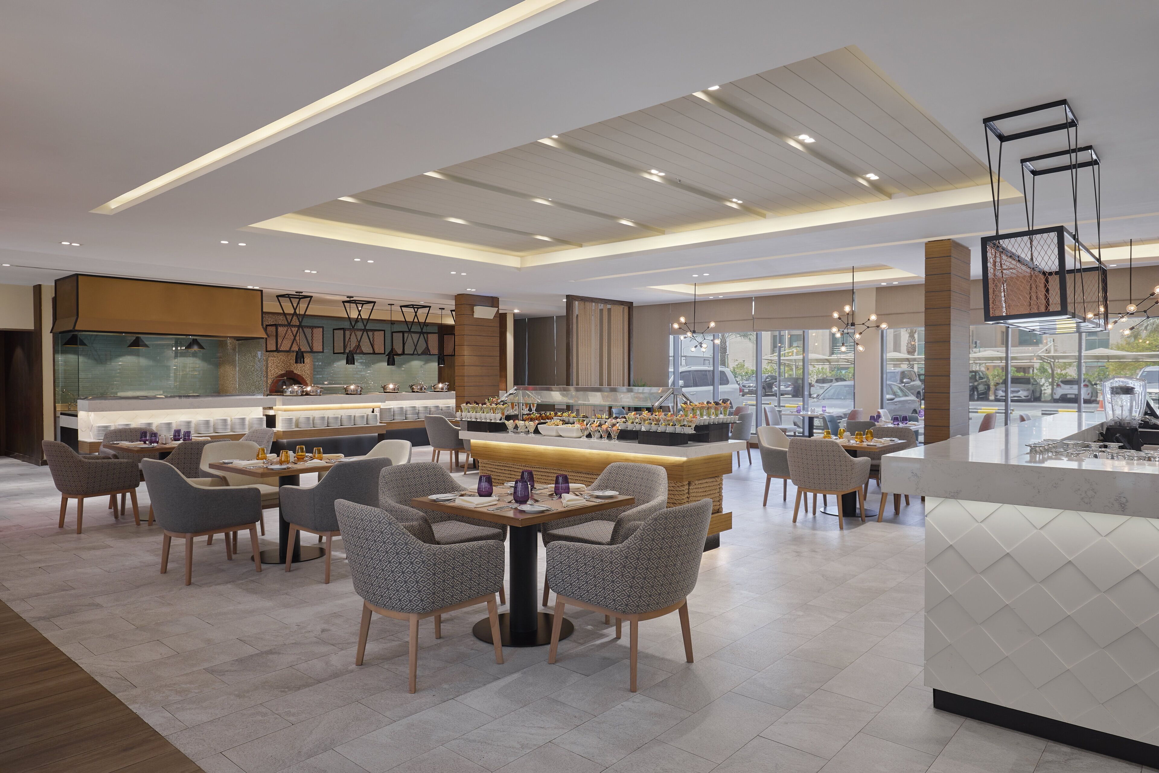 A modern restaurant with a central bar area, multiple seating options, and a view of the street through large windows.