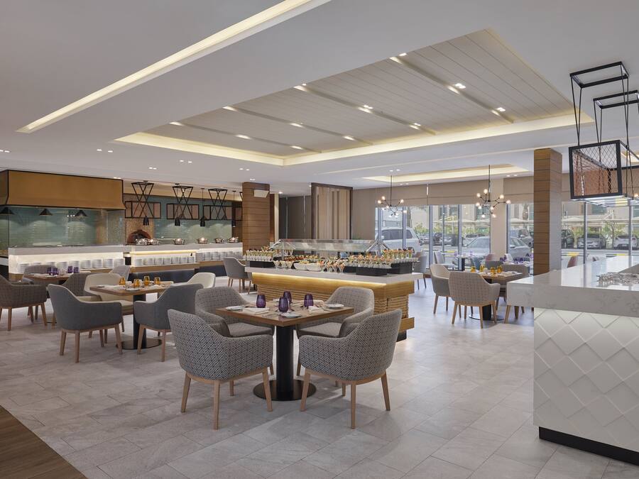 A modern restaurant with a central bar area, multiple seating options, and a view of the street through large windows.