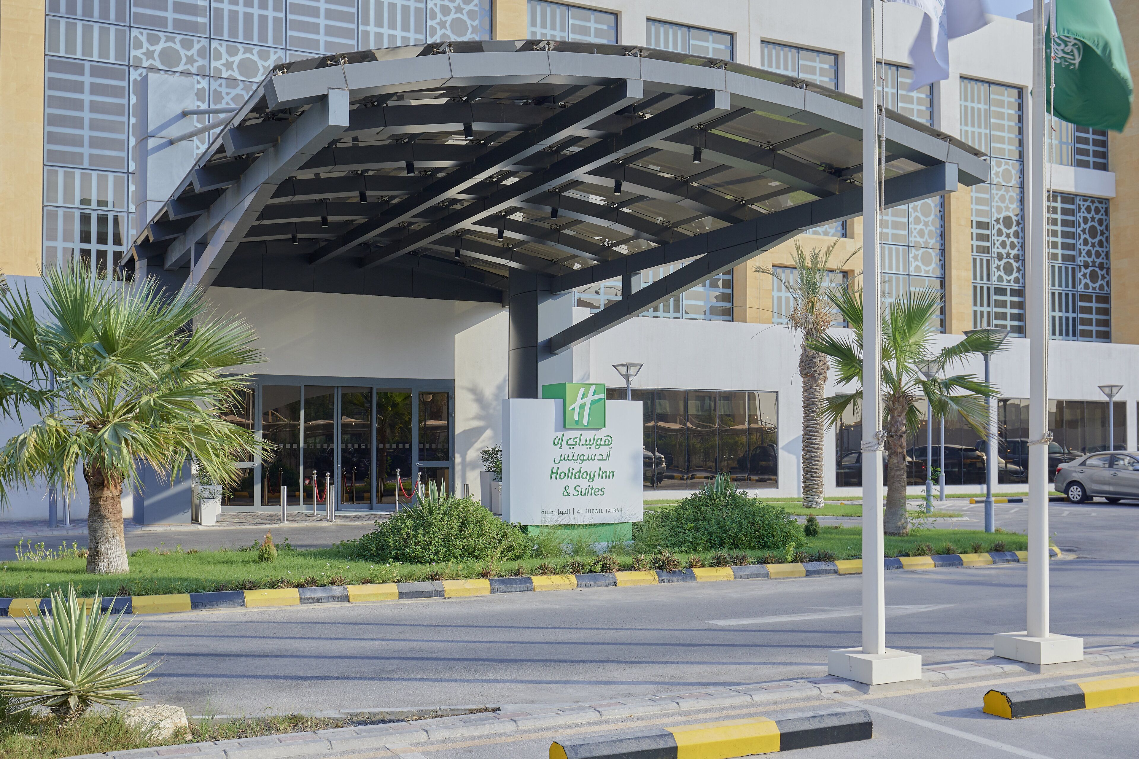A Holiday Inn with a covered entrance, palm trees, and a clear sky.