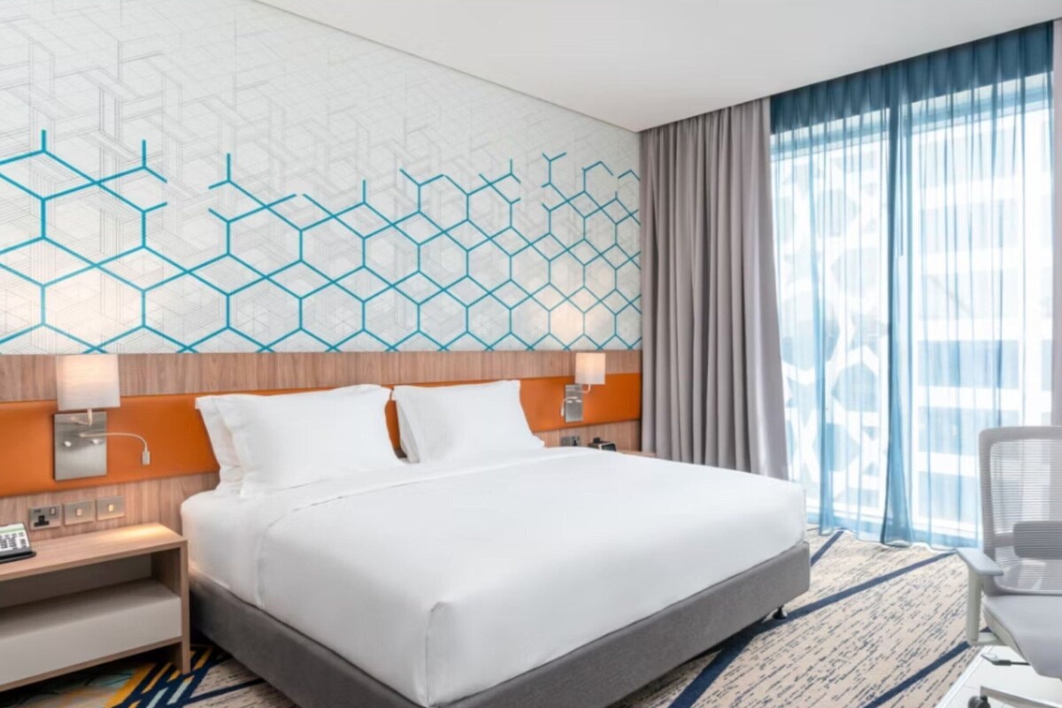 Habitación de hotel con una cama grande, un escritorio con teléfono, una silla, un televisor y una ventana con cortinas.
