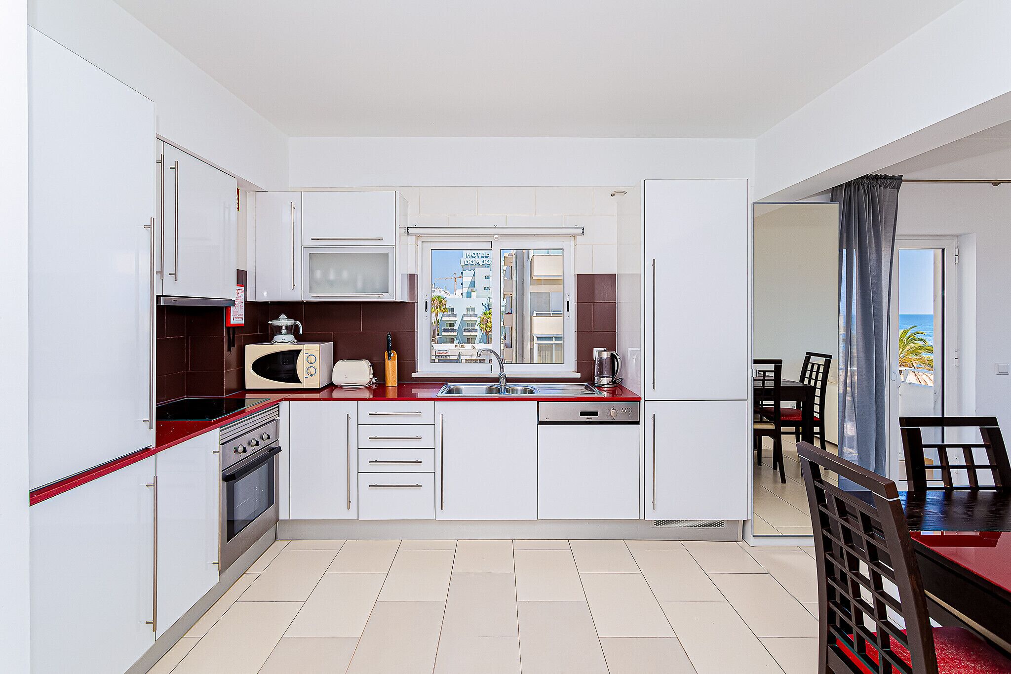 A modern kitchen with white cabinets, a red countertop, and a view of the city through the window.