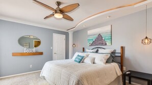 Ein Schlafzimmer mit Bett, Deckenventilator, Gemälde, Spiegel und einem kleinen Tisch.