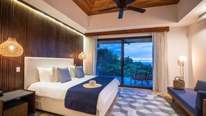 Un dormitorio con una cama grande, ventilador de techo, vistas al exterior y una zona de estar con una lámpara.