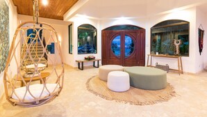 Amplia habitación con una silla colgante, otomanes, techo de madera y ventanas grandes con arcos.