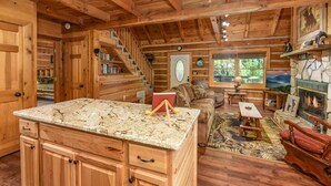 A log cabin interior with a kitchen area, a fireplace, a sofa, and a staircase. - Free Tickets | Private Balcony, Grill, Game Room, Hot Tub, Great Location (Sevierville)