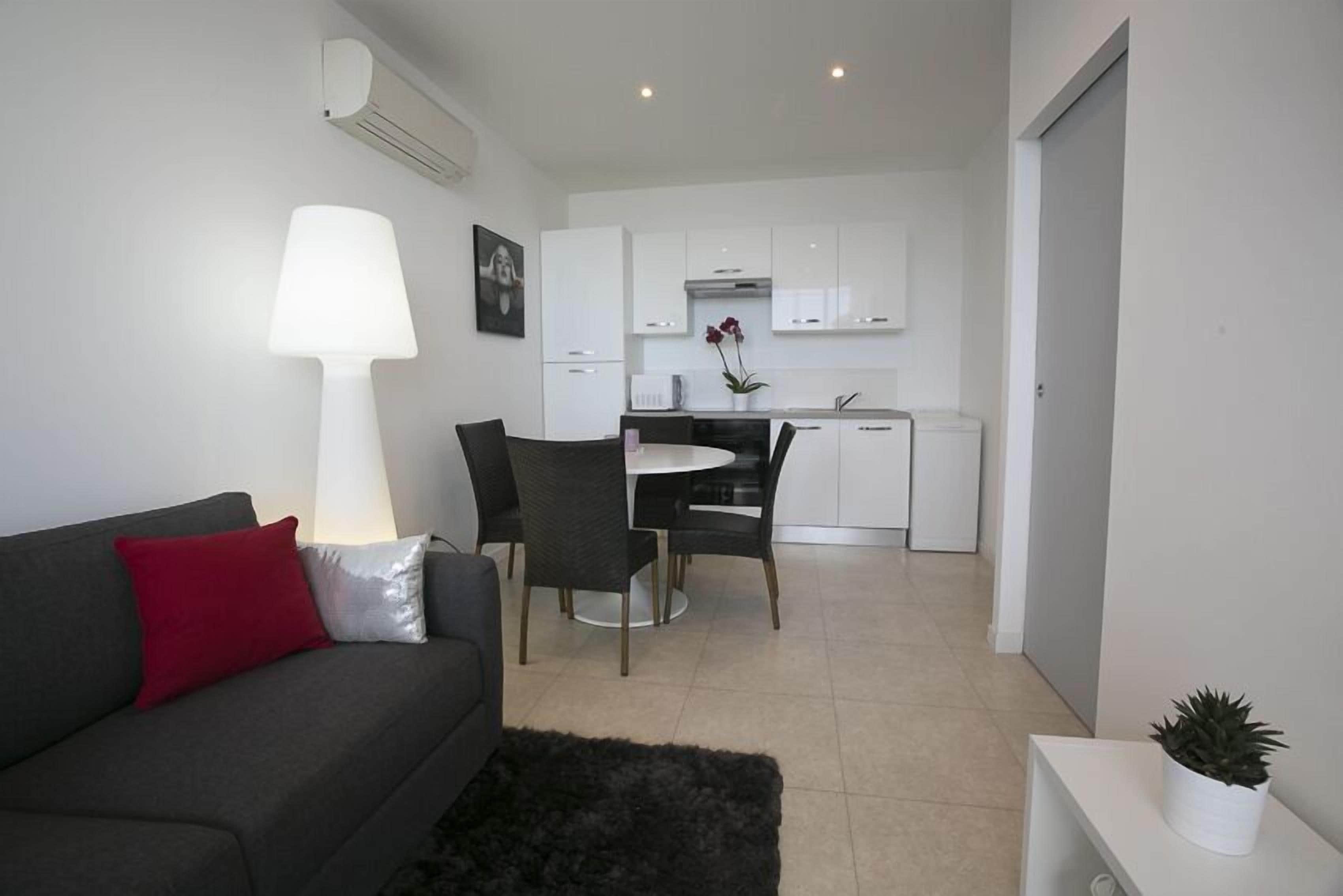 A modern living room with a grey sofa, a black rug, and a dining area with a white table and chairs.