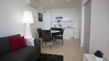 A modern living room with a grey sofa, a black rug, and a dining area with a white table and chairs.