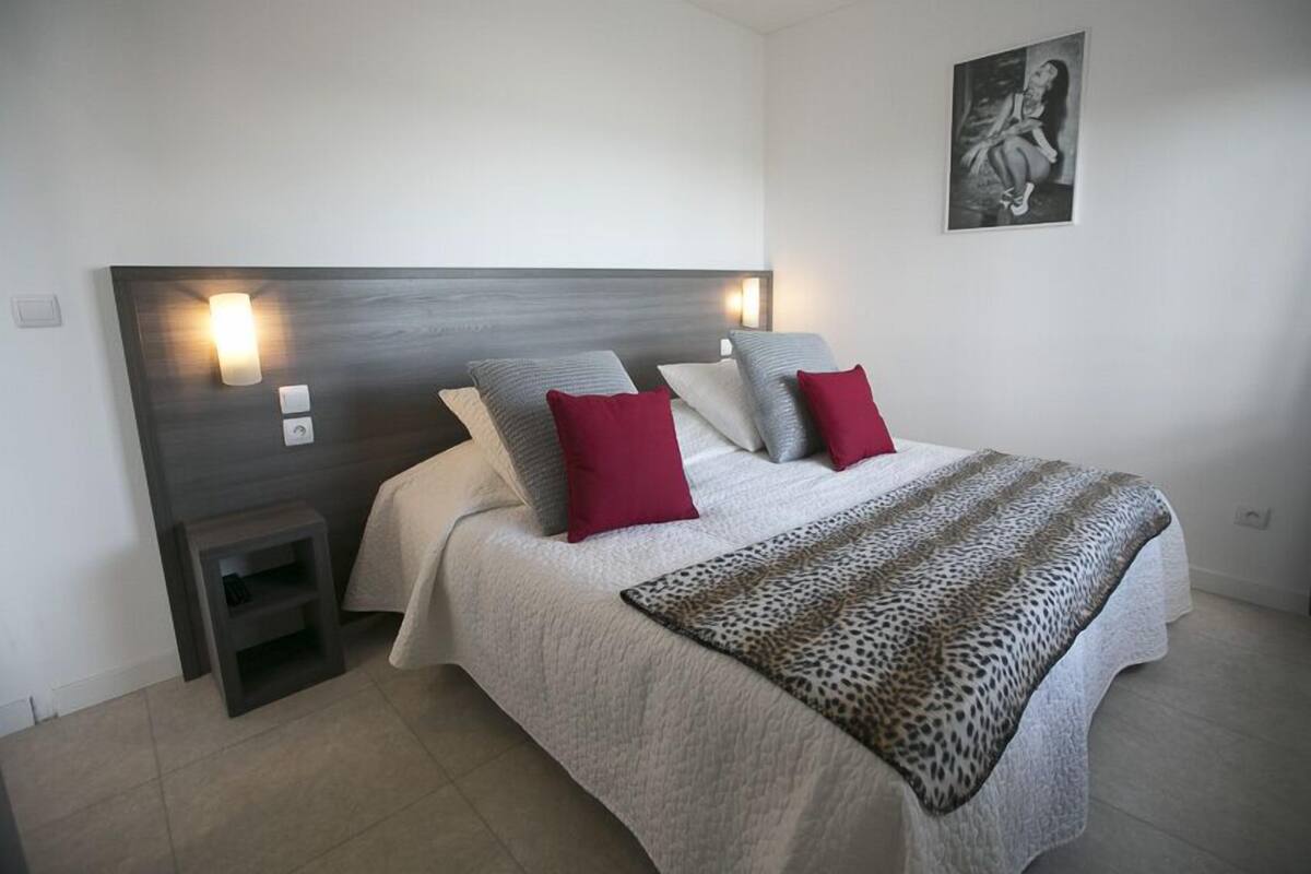 Ein Schlafzimmer mit einem großen Bett, zwei Nachttischen, einem Beistelltisch, einem Kopfteil mit Wandleuchten und einem gerahmten Bild an der Wand.