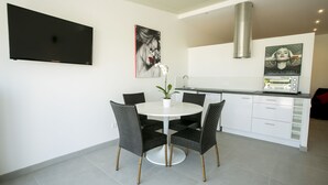 A modern kitchen with a flat-screen TV, a painting, a toaster oven, and a dining area with a round table and chairs.