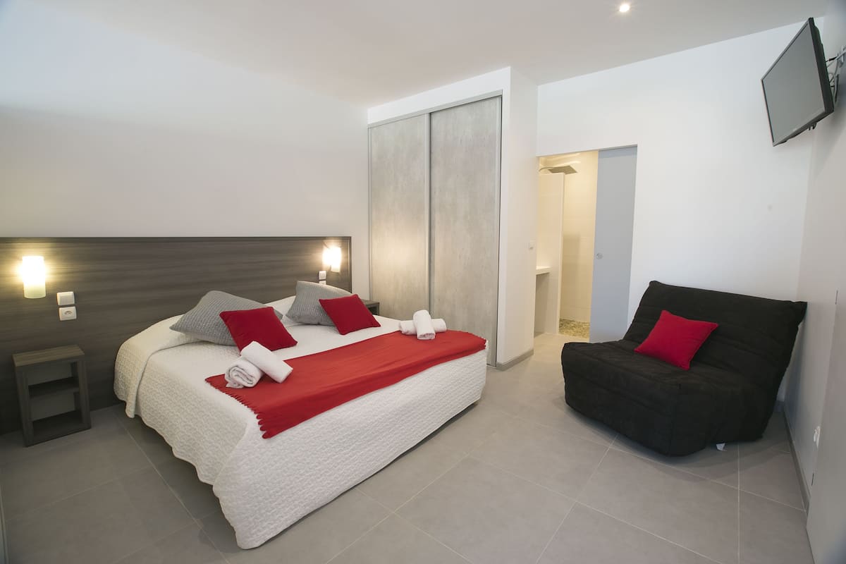 Ein modernes Hotelzimmer mit einem großen Bett, einer Couch, einem an der Wand befestigten Fernseher und einem Schiebetürenschrank.
