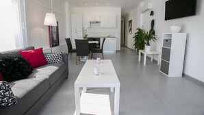 A modern living room with a grey sofa, white coffee table, and a dining area with a white table and chairs.