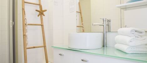 Een badkamer met een glazen wastafel, witte kastjes en een houten ladder die tegen de muur staat.