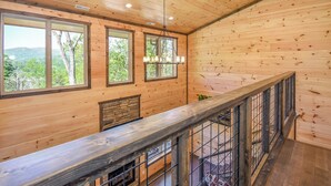 A wooden cabin interior with large windows, a fireplace, and a balcony with a railing.