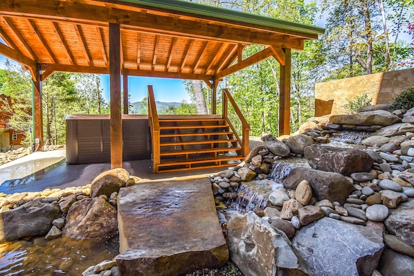 Un quiosco de madera con una fuente de piedra y un jacuzzi.