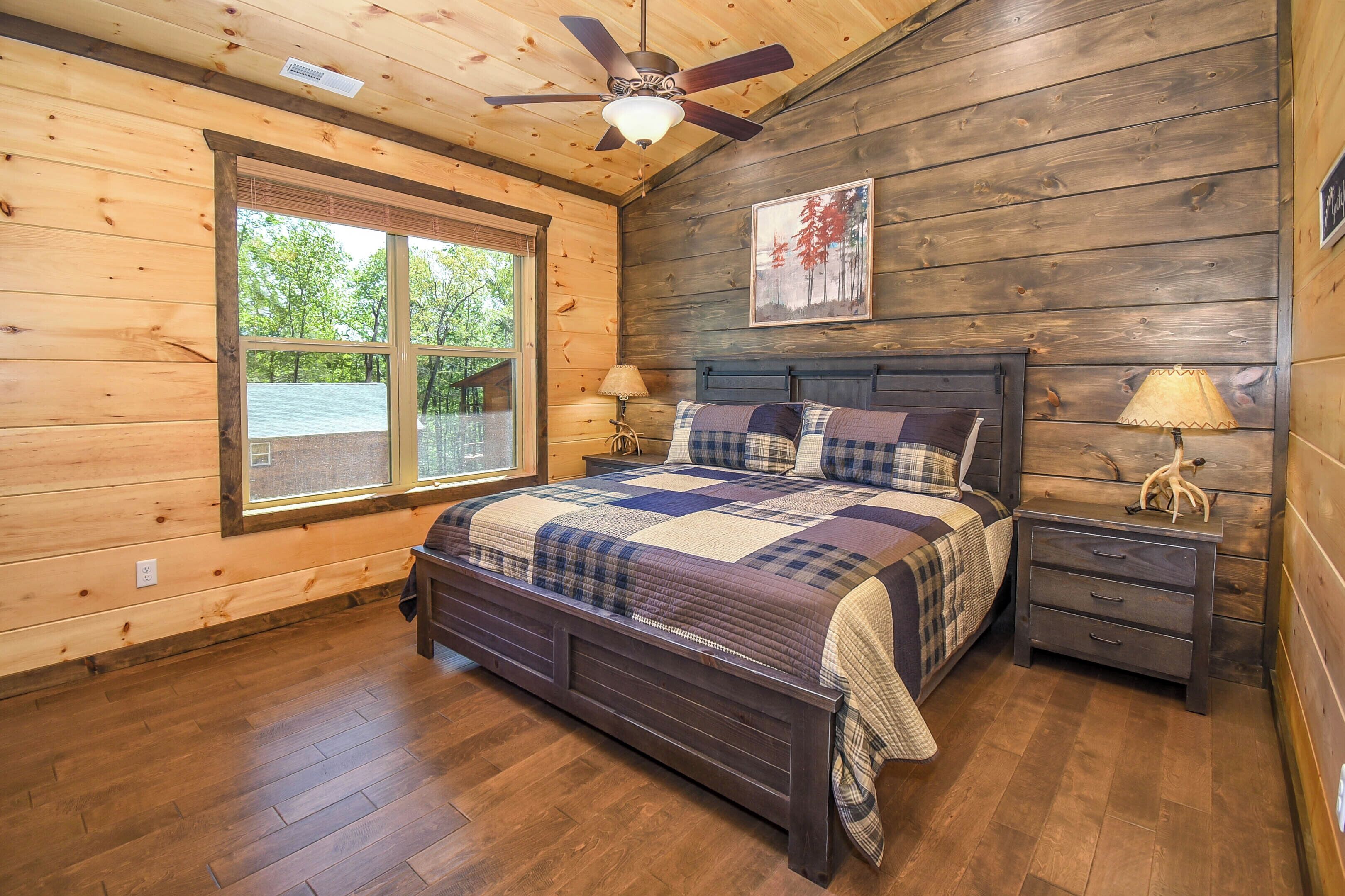 Een slaapkamer met houten lambrisering, een bed, een plafondventilator, een raam en een nachtkastje.