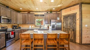 A wooden cabin-style kitchen with a central island, bar stools, a refrigerator, a microwave, and a coffee station.