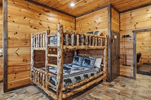 Interior rústico de una cabaña de madera con una cama de madera escalonada y un edredón con motivos de osos.