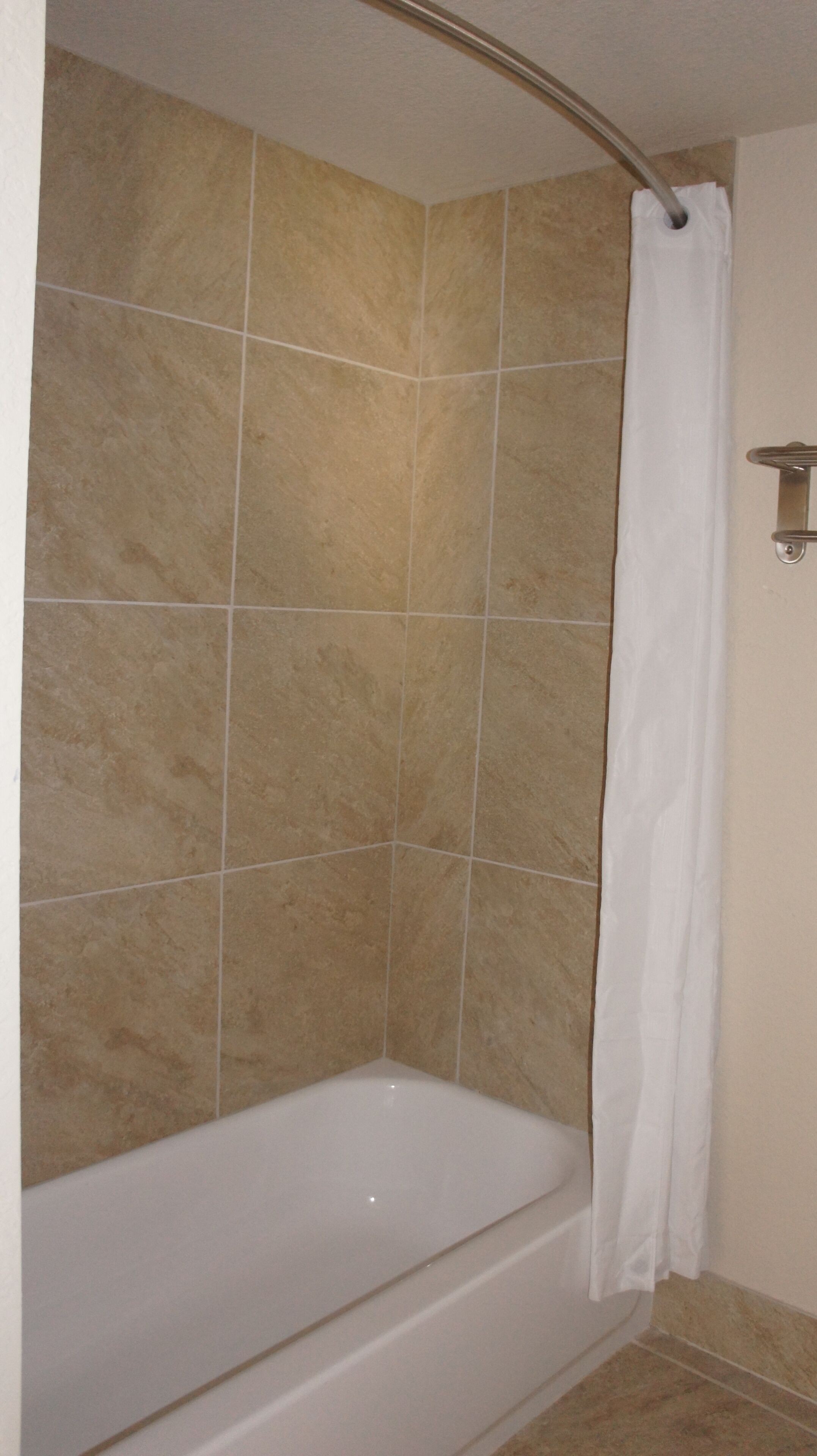 Un baño con bañera, paredes de azulejos color crema y cortina de ducha blanca.