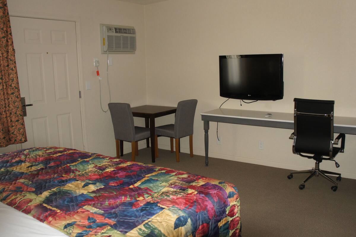 A hotel room with a bed, a desk, a chair, a television, and a refrigerator.