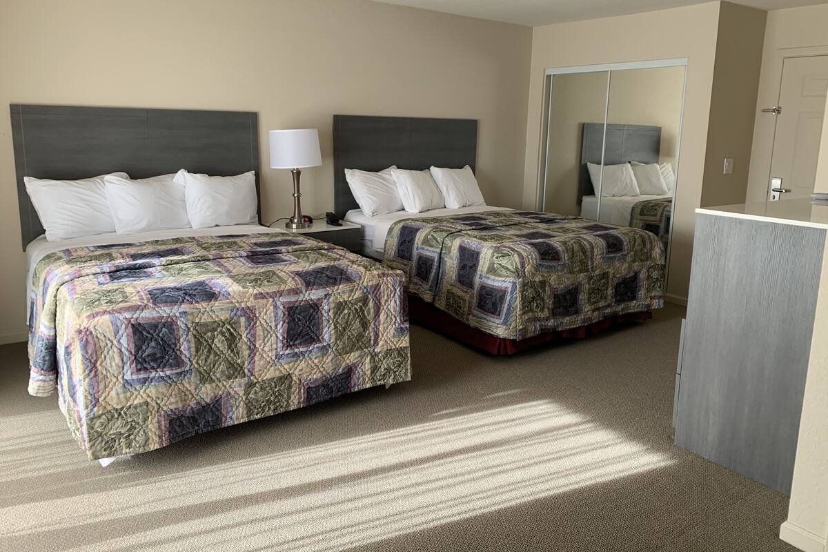 A hotel room with two beds, a nightstand, a lamp, a mirror, and a wardrobe.