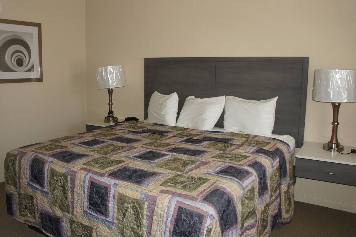 A hotel room with a large bed, two bedside lamps, a headboard, and a framed picture on the wall.