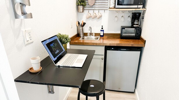 Cocina compacta con una laptop sobre una encimera negra, un fregadero, un microondas y un refrigerador pequeño.