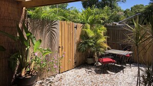 Una estructura de pérgola de madera con un patio de grava, plantas en macetas y un juego de mesa y sillas rojo para exteriores.
