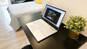 Una computadora portátil sobre un escritorio, con una cama al fondo.