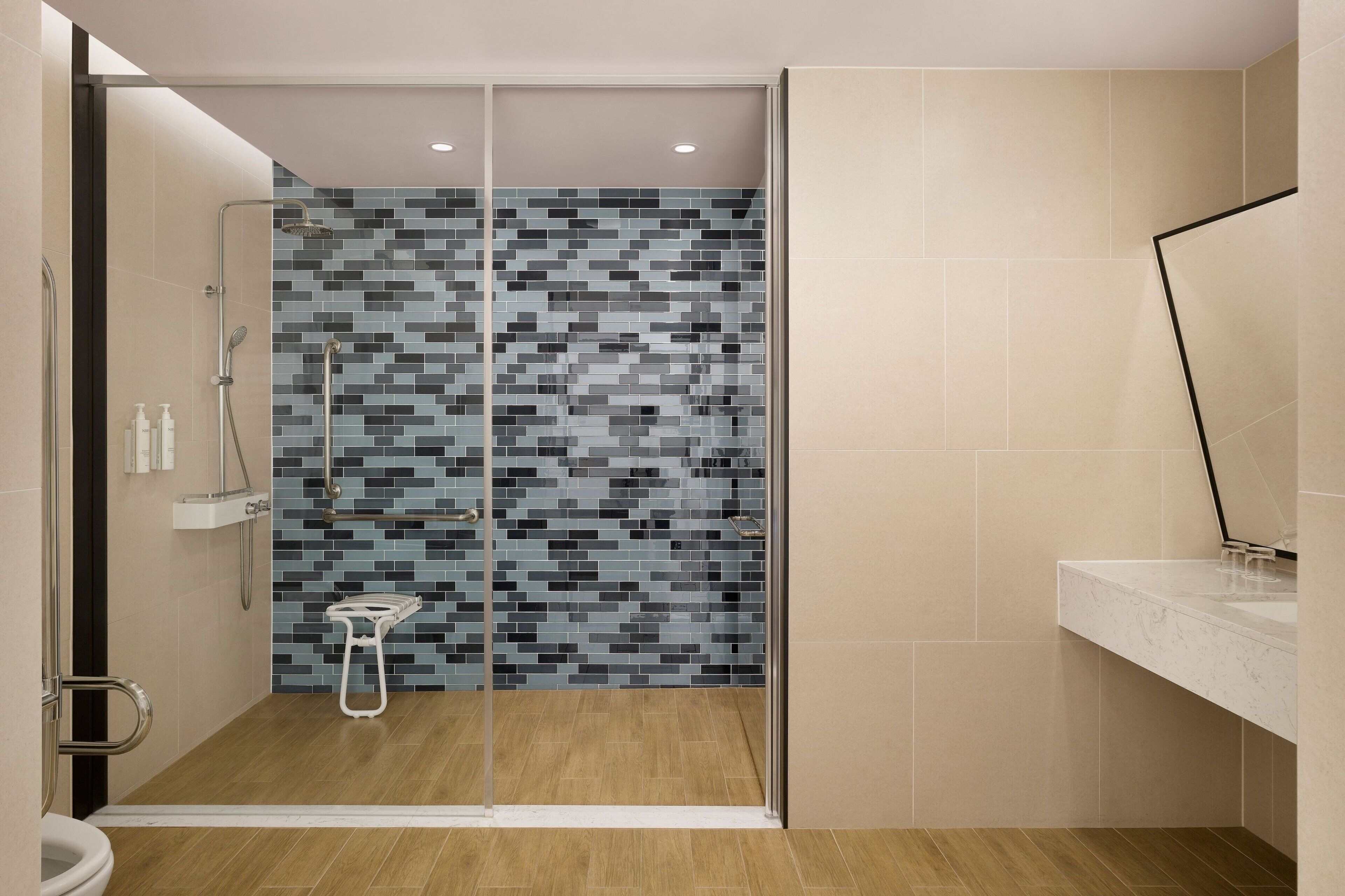 A modern bathroom with a glass shower enclosure, a tiled shower wall, and a wooden floor.