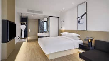 Une chambre d’hôtel moderne dotée d’un grand lit, d’un téléviseur à écran plat, d’une table de chevet avec une lampe et d’un grand tableau abstrait accroché au mur.