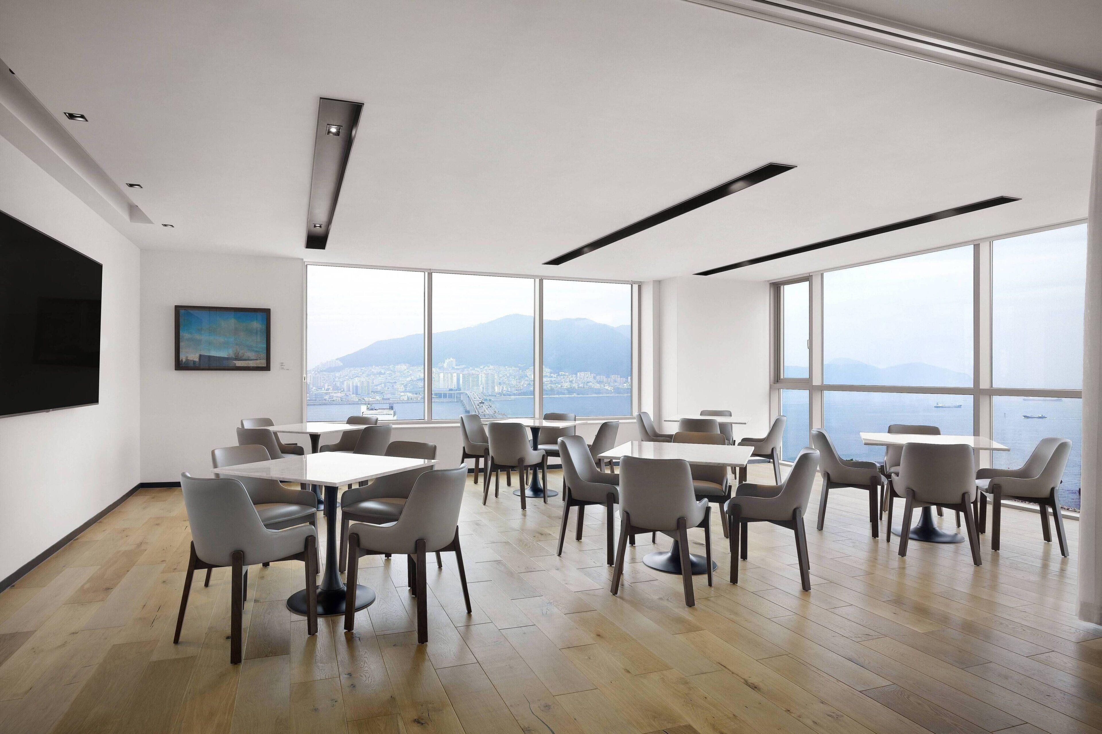 A modern conference room with large windows, wooden flooring, and a cityscape view.