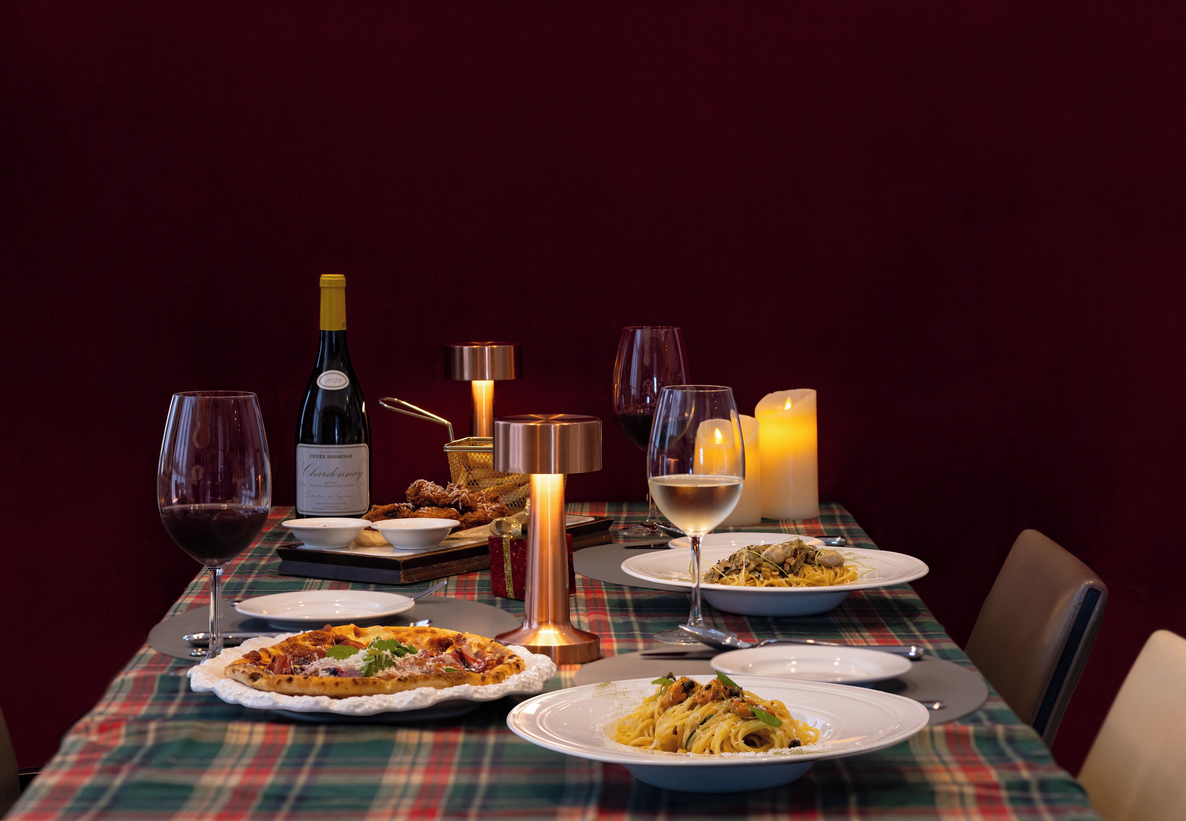 A dining table set with plates of food, wine glasses, a bottle of wine, and candles.