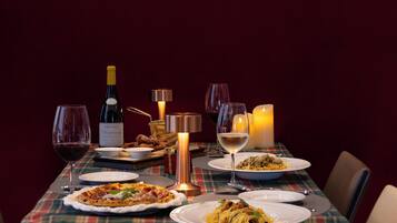 Una mesa de comedor dispuesta con platos de comida, copas de vino, una botella de vino y velas.