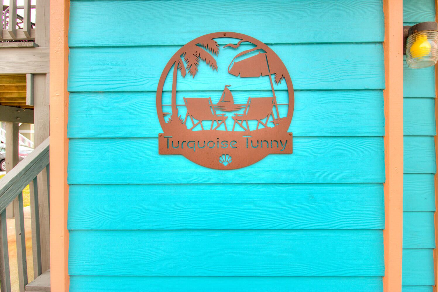 Un mur en bois turquoise orné d’un logo circulaire représentant un palmier, un voilier et le texte « Turquoise Tunny ».