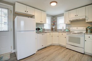 Compact kitchen with modern design, featuring white cabinetry, refrigerator, microwave, and stove.