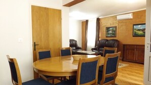 A dining area with a round wooden table and six chairs, a leather sofa, and a wooden cabinet. - GARDEN APARTMENT with 3 bedrooms (Budva)