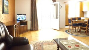 A living room with a leather sofa, a television, a dining table with chairs, and a patterned rug. - GARDEN APARTMENT with 3 bedrooms (Budva)