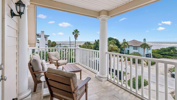 A covered balcony with a view of the ocean, a white railing, and a seating area with two chairs and a table. - Magnificent Ocean Views, Private Heated Pool, Billards on East Beach! (Saint Simons Island)