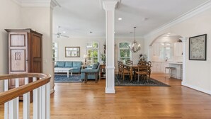 A spacious living room with hardwood floors, a dining area with a chandelier, and a kitchen with white cabinetry. - Magnificent Ocean Views, Private Heated Pool, Billards on East Beach! (Saint Simons Island)