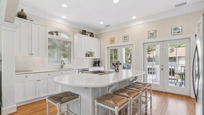 A kitchen with white cabinetry, a large island with bar stools, and a view to the outside. - Magnificent Ocean Views, Private Heated Pool, Billards on East Beach! (Saint Simons Island)