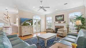 A spacious living room with a television, sofa, armchair, fireplace, and a staircase. - Magnificent Ocean Views, Private Heated Pool, Billards on East Beach! (Saint Simons Island)