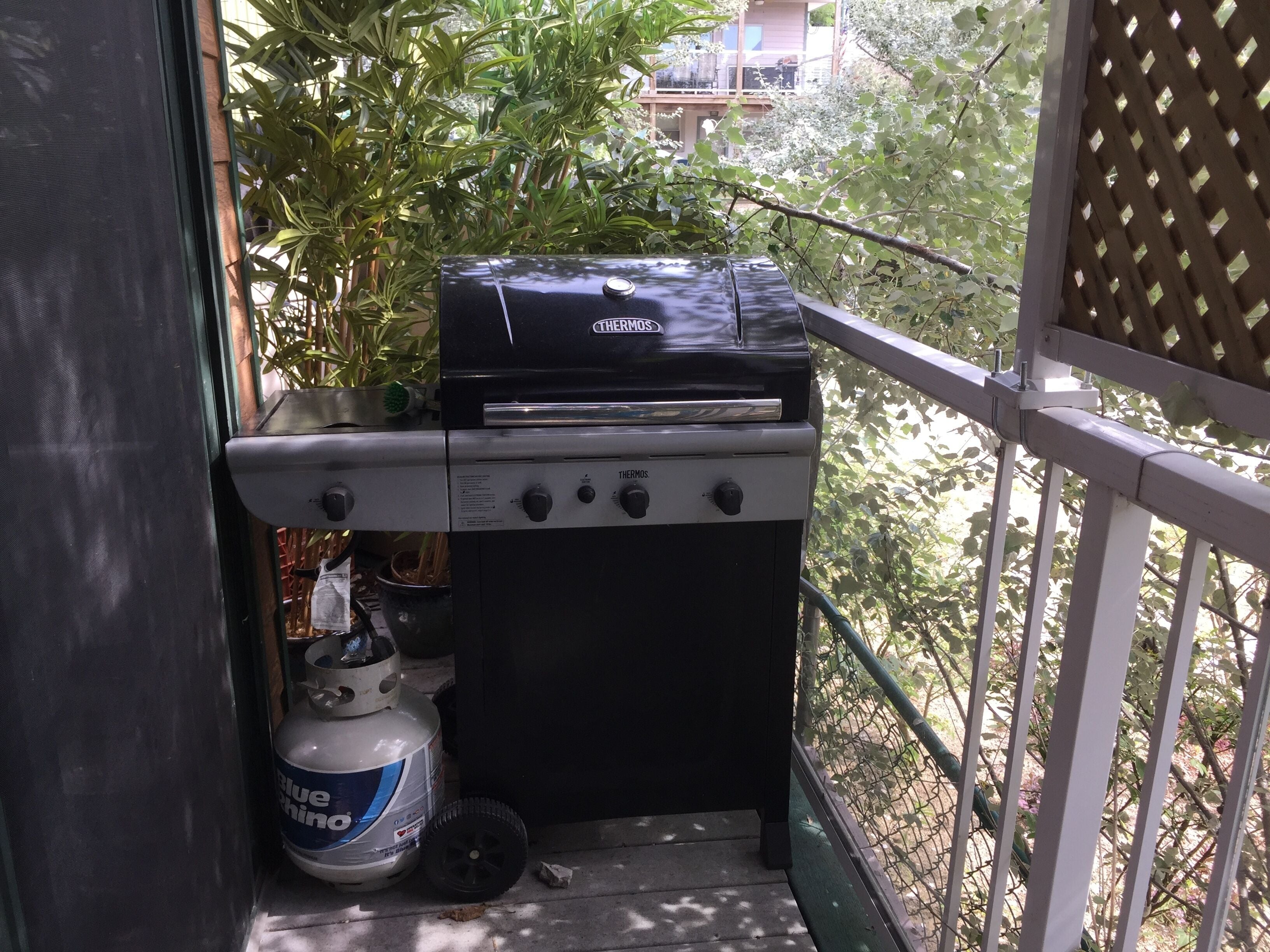 Un barbecue Thermos noir avec une bouteille de propane sur un balcon.