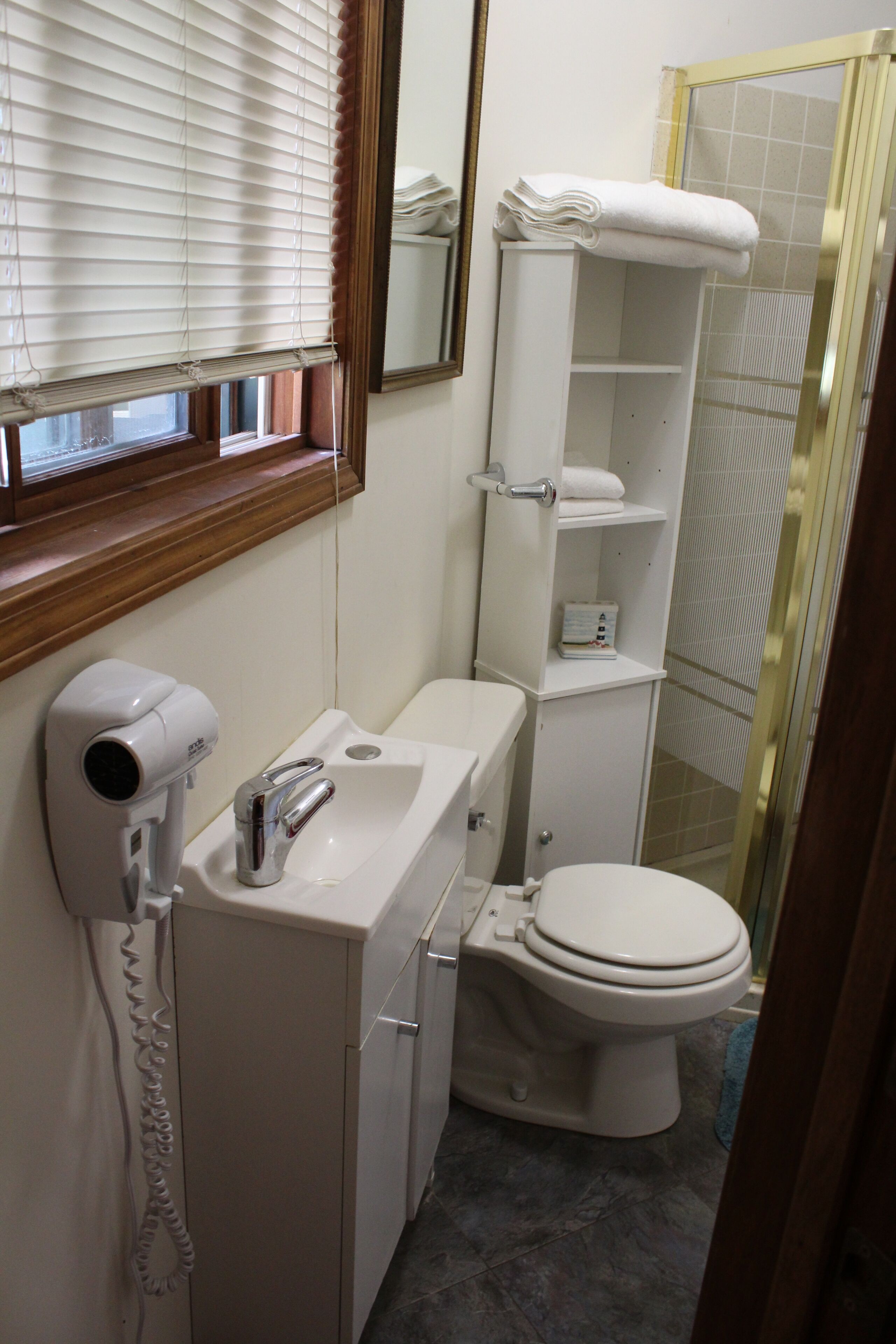 Un baño con lavamanos blanco, secador de pelo, inodoro y zona de ducha.